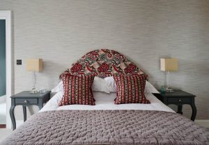 Nina Campbell Patterened Shaped Headboard. with reds and blues with 4 cushions in red hues on a guest bed.